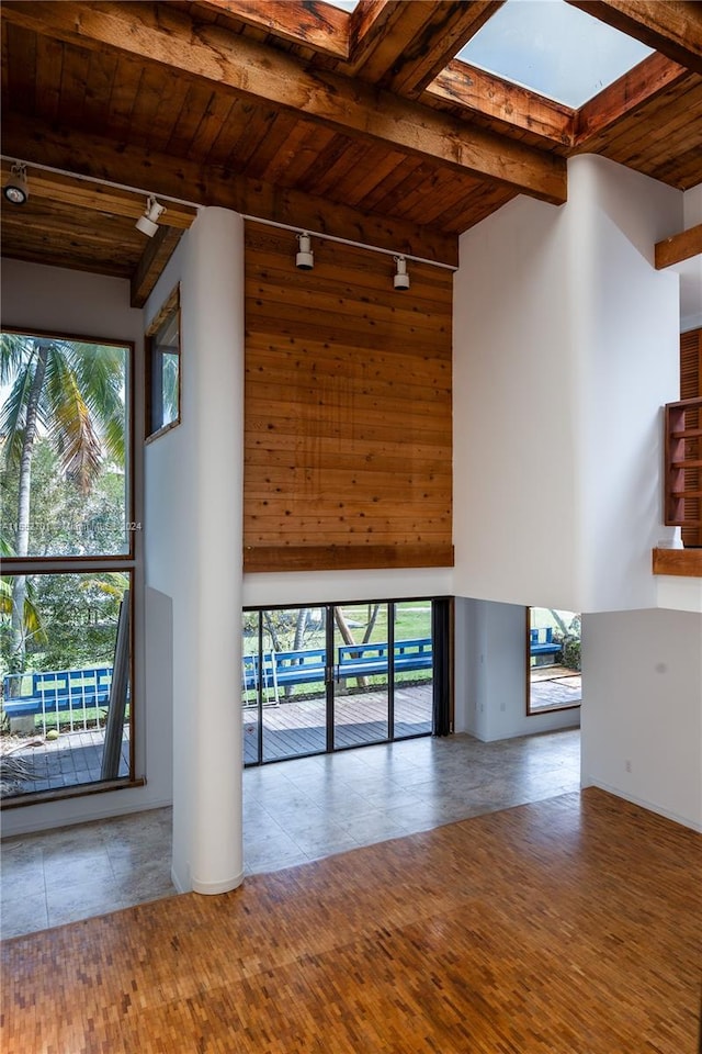 unfurnished living room with high vaulted ceiling, beamed ceiling, a skylight, and wooden ceiling