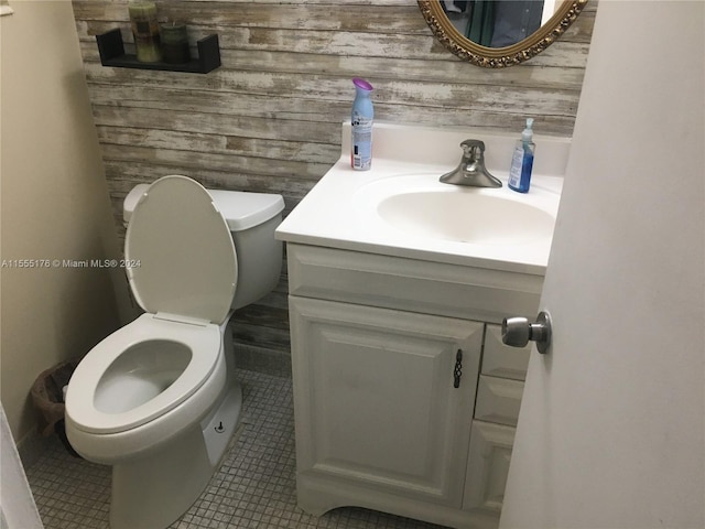 bathroom with wooden walls, tile flooring, vanity with extensive cabinet space, and toilet