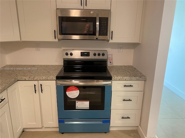 kitchen with light tile floors, white cabinetry, appliances with stainless steel finishes, and light stone countertops