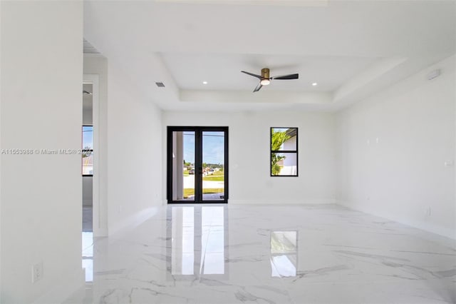 tiled empty room with ceiling fan and a raised ceiling