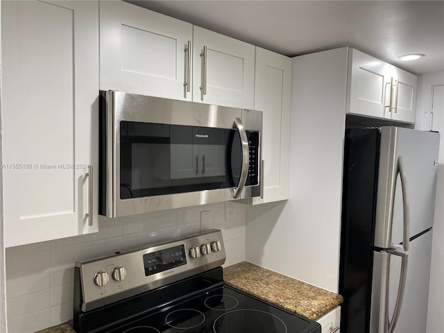 kitchen featuring appliances with stainless steel finishes, white cabinetry, dark stone counters, and backsplash