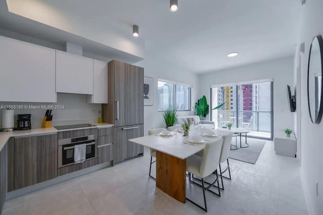 kitchen featuring light tile floors, a kitchen bar, white cabinetry, and stainless steel oven