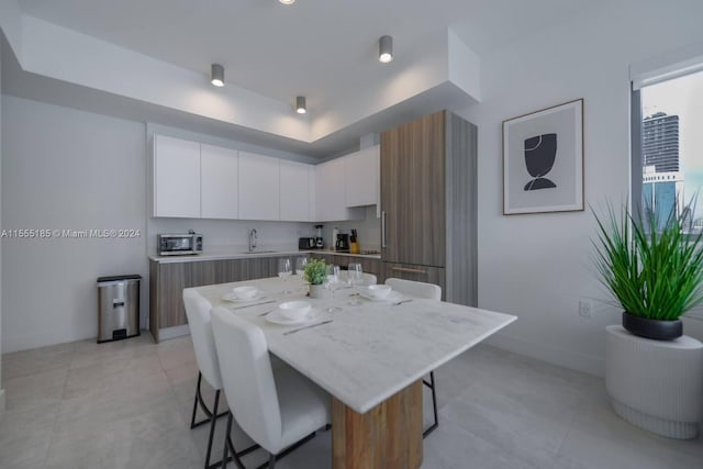 kitchen with light tile flooring, a kitchen breakfast bar, a kitchen island, and white cabinetry