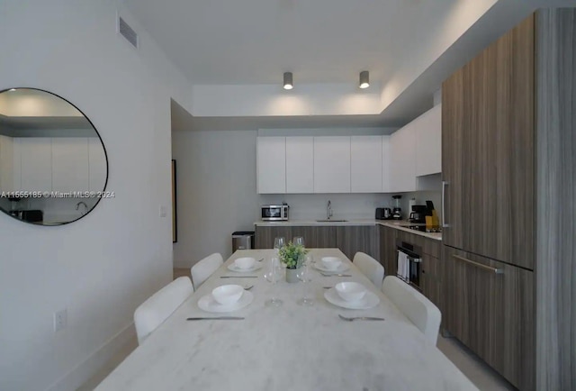 kitchen with a kitchen breakfast bar, a kitchen island, white cabinetry, sink, and light stone counters