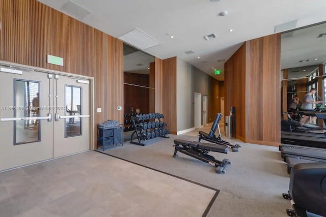 exercise room featuring french doors, wooden walls, light colored carpet, and a high ceiling