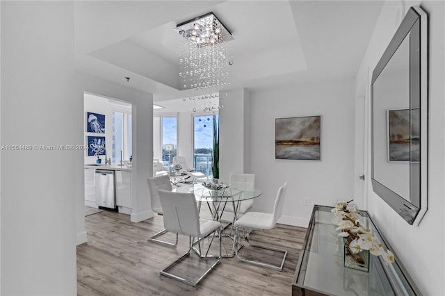 dining area featuring a raised ceiling, light hardwood / wood-style flooring, and an inviting chandelier