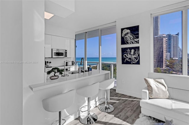 interior space with sink, light hardwood / wood-style flooring, a water view, a kitchen bar, and white cabinetry