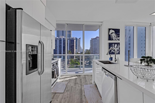 kitchen featuring expansive windows, light hardwood / wood-style flooring, white cabinetry, appliances with stainless steel finishes, and sink