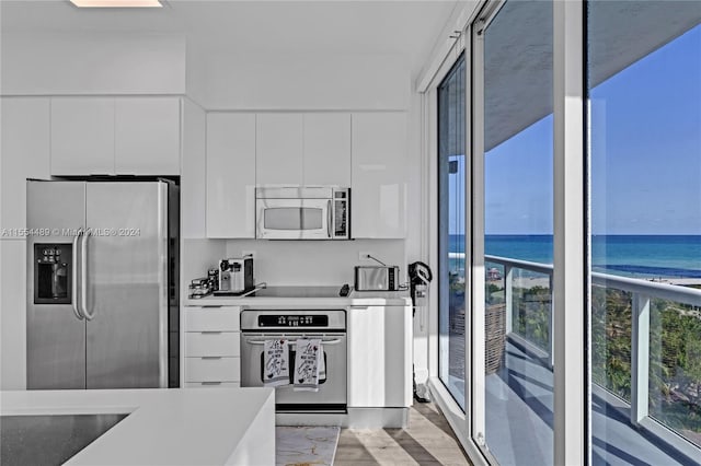 kitchen with white cabinets, a water view, stainless steel appliances, and light hardwood / wood-style floors