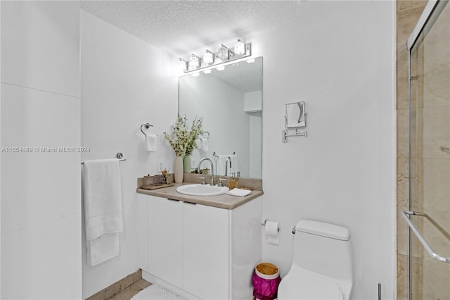 bathroom with a textured ceiling, a shower with shower door, large vanity, and toilet