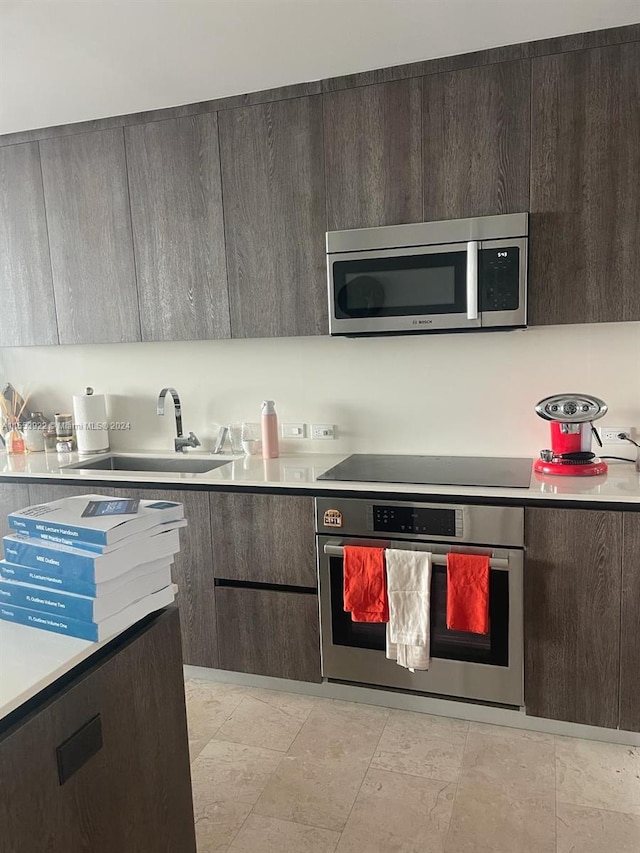 kitchen with appliances with stainless steel finishes, dark brown cabinets, sink, and light tile flooring