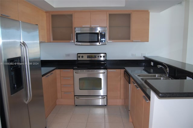 kitchen with light tile floors, kitchen peninsula, dark stone counters, and stainless steel appliances