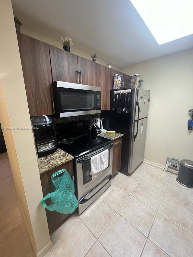 kitchen with light tile flooring, light stone countertops, dark brown cabinetry, and appliances with stainless steel finishes