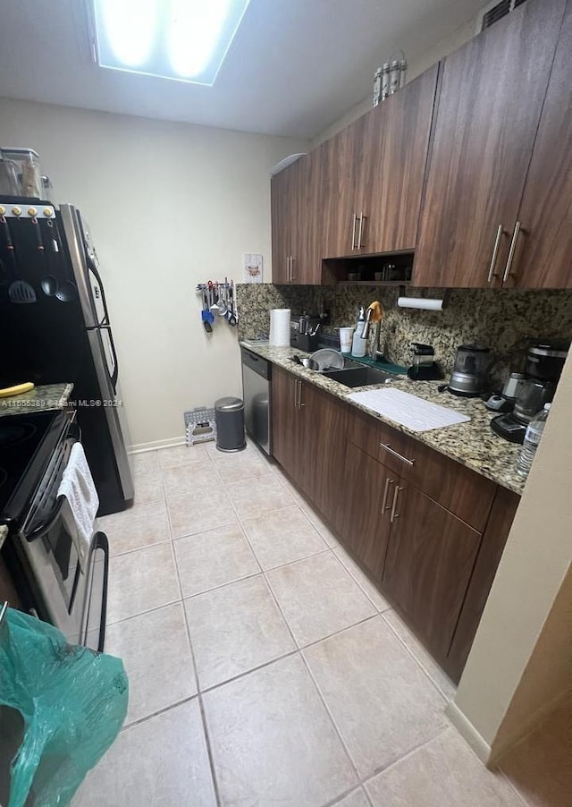 kitchen with light tile floors, dishwashing machine, tasteful backsplash, dark brown cabinets, and light stone counters