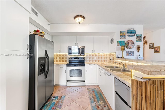 kitchen featuring stainless steel appliances, light tile floors, tasteful backsplash, white cabinetry, and sink