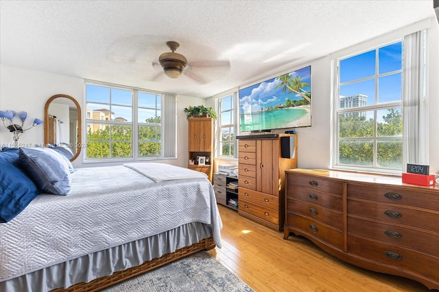 bedroom with a textured ceiling, ceiling fan, multiple windows, and light wood-type flooring