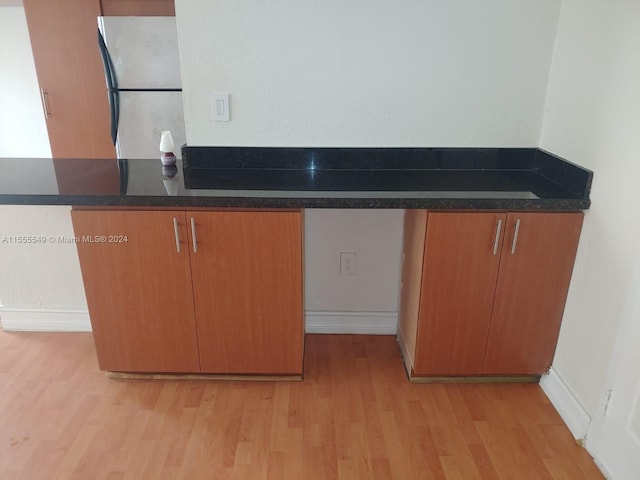 kitchen with dark stone countertops, stainless steel refrigerator, and light hardwood / wood-style flooring