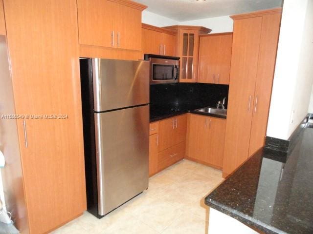 kitchen with stainless steel appliances, light tile flooring, dark stone countertops, and sink