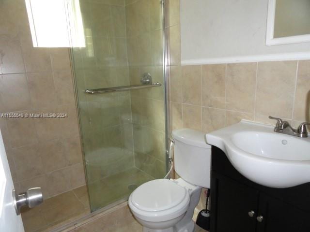 bathroom featuring backsplash, tile walls, oversized vanity, toilet, and a shower with shower door