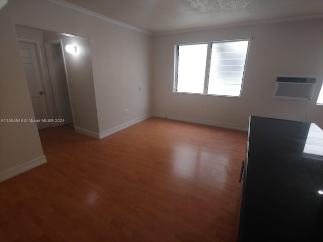 empty room featuring a wall mounted AC, light wood-type flooring, and crown molding