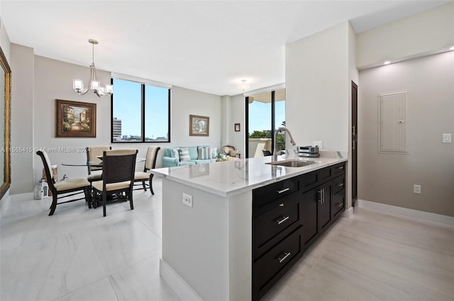 kitchen with light stone countertops, a wall of windows, a notable chandelier, sink, and pendant lighting