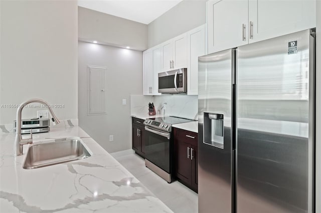 kitchen with light tile flooring, appliances with stainless steel finishes, white cabinets, light stone counters, and sink