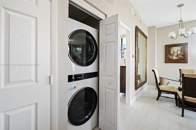 laundry area featuring a notable chandelier, stacked washer / dryer, and light tile flooring