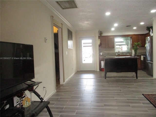 kitchen featuring a textured ceiling, light wood-type flooring, ornamental molding, and stainless steel refrigerator