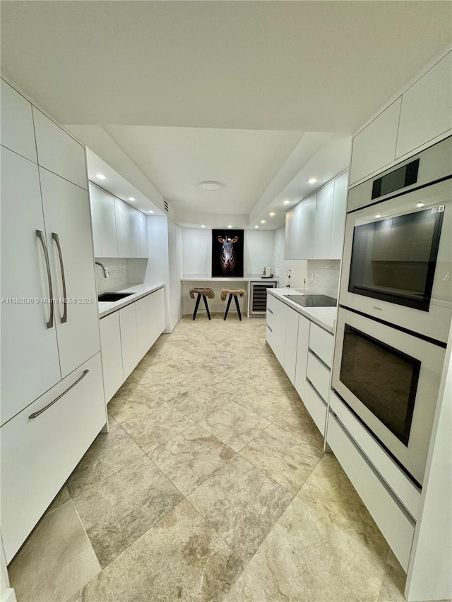 kitchen with white double oven, sink, white cabinets, and black electric cooktop