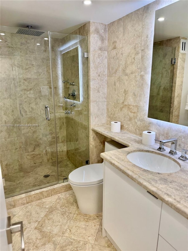 bathroom with a shower with shower door, vanity, tile walls, and toilet