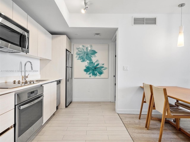 kitchen with decorative light fixtures, white cabinetry, appliances with stainless steel finishes, sink, and rail lighting