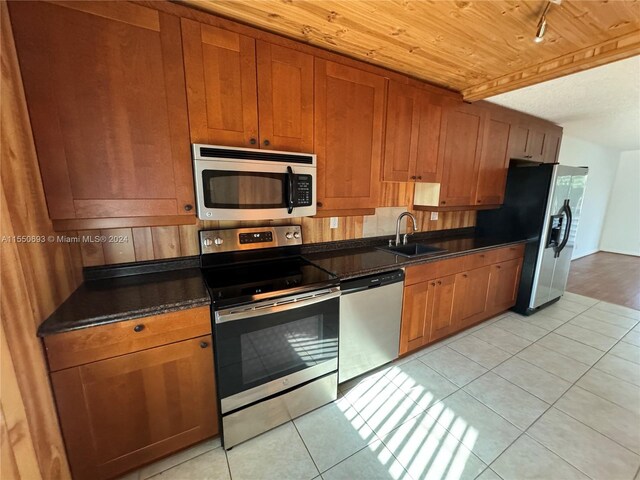 kitchen featuring dark stone countertops, appliances with stainless steel finishes, wooden ceiling, sink, and light tile flooring