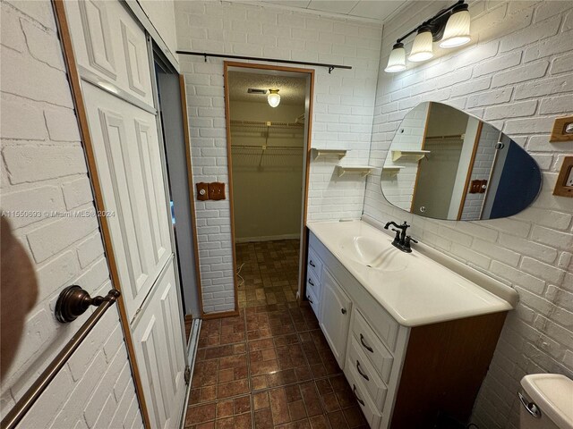 bathroom featuring brick wall, tasteful backsplash, toilet, and vanity with extensive cabinet space