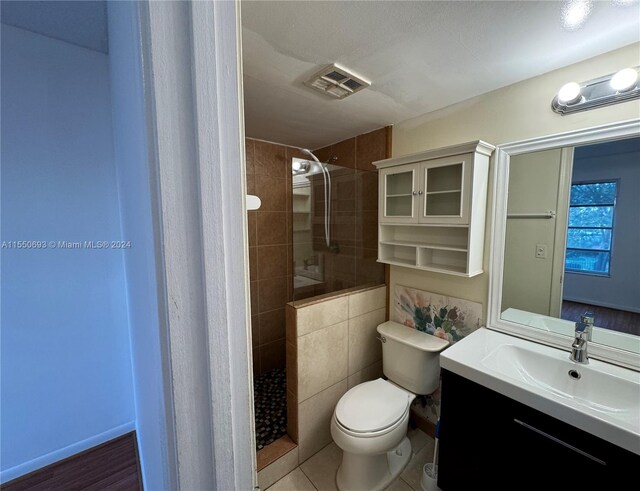 bathroom with tile flooring, a tile shower, tile walls, large vanity, and toilet