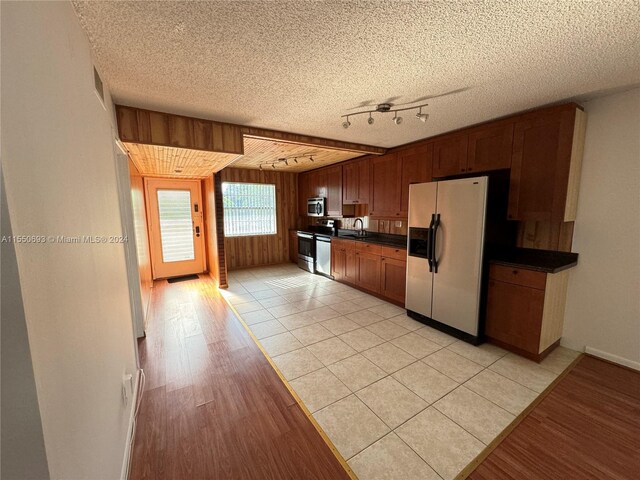 kitchen featuring light hardwood / wood-style flooring, wood walls, rail lighting, appliances with stainless steel finishes, and a textured ceiling