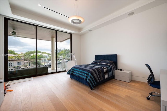 bedroom featuring expansive windows, access to outside, hardwood / wood-style floors, and a tray ceiling