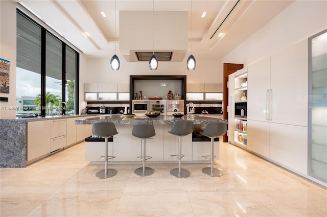 kitchen with light tile patterned floors, pendant lighting, a center island with sink, and a tray ceiling