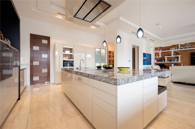 kitchen with light tile patterned flooring, a large island, stone countertops, decorative light fixtures, and sink