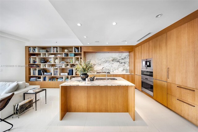 kitchen with light tile patterned floors, appliances with stainless steel finishes, sink, and a center island with sink