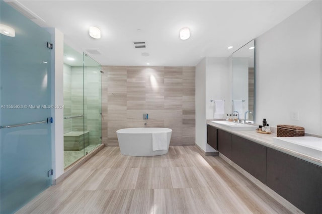 bathroom with tile walls, shower with separate bathtub, double sink vanity, and tile patterned floors