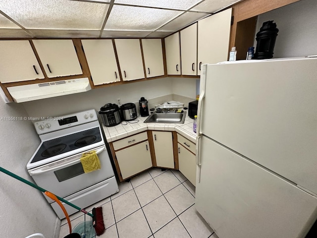 kitchen featuring white appliances, sink, a paneled ceiling, light tile floors, and tile counters