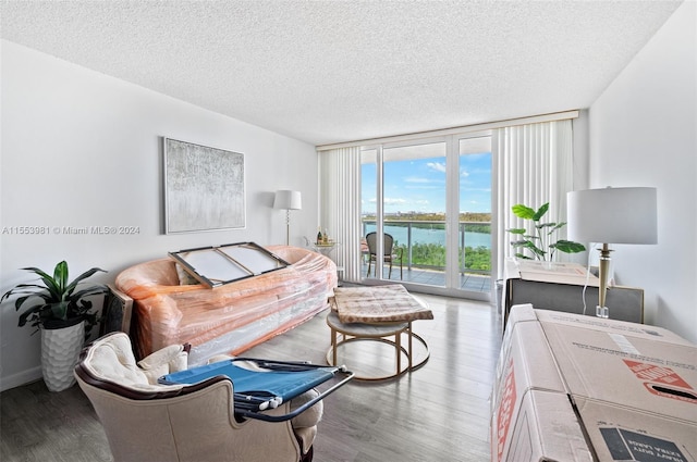 living room featuring a textured ceiling, floor to ceiling windows, hardwood / wood-style flooring, and a water view