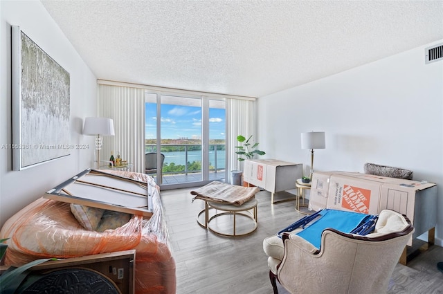 living room with a water view, expansive windows, a textured ceiling, and hardwood / wood-style flooring