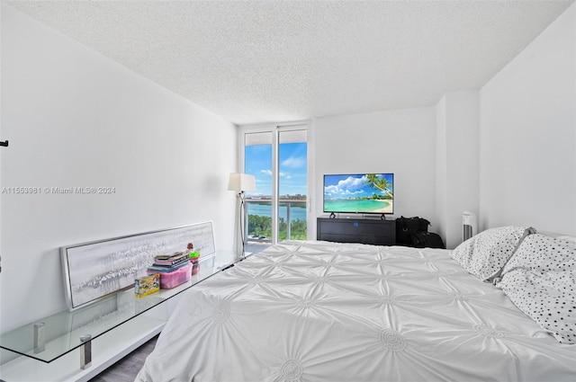 bedroom with floor to ceiling windows, a water view, access to outside, and a textured ceiling