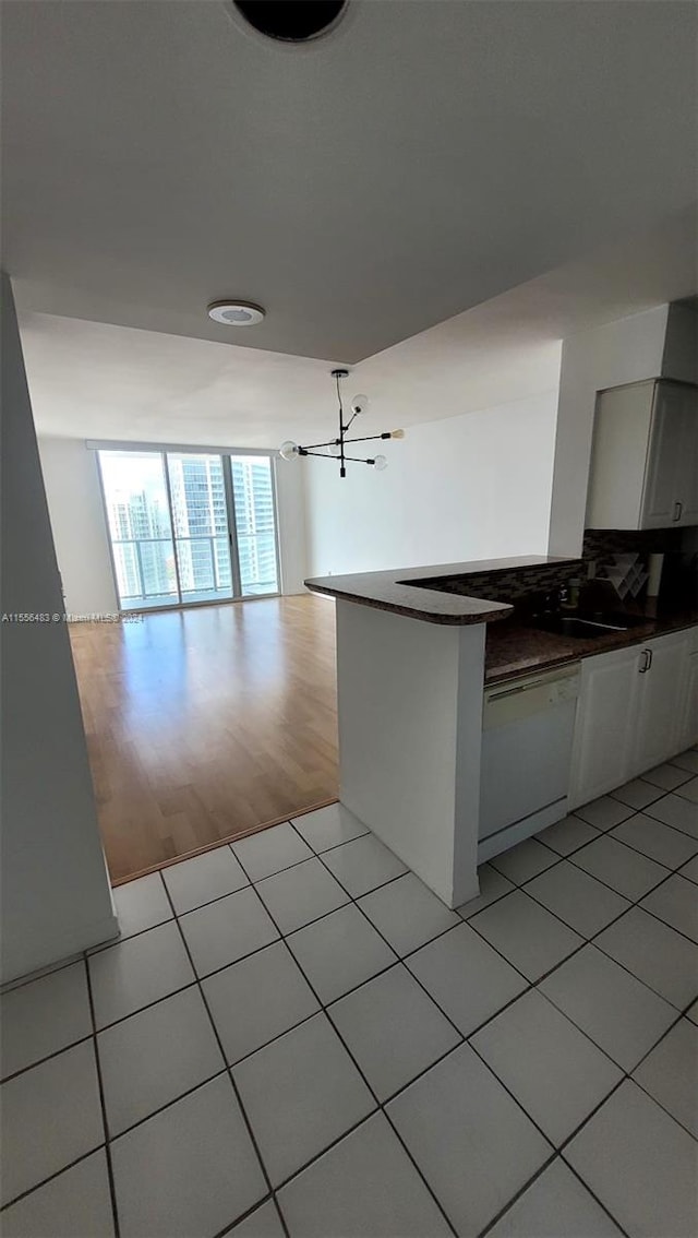 kitchen featuring light tile floors, tasteful backsplash, white cabinetry, a wall of windows, and dishwasher