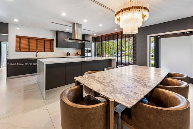 kitchen featuring a large island, wall chimney exhaust hood, sink, and an inviting chandelier