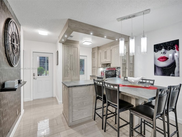 kitchen featuring a breakfast bar area, hanging light fixtures, a textured ceiling, and white cabinets