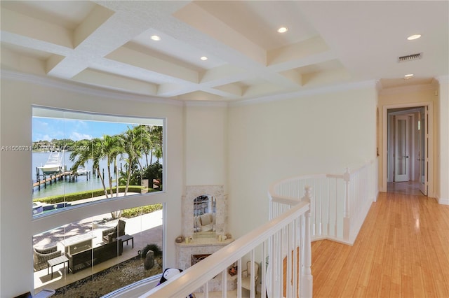 hallway with a water view, coffered ceiling, a healthy amount of sunlight, and light wood-type flooring