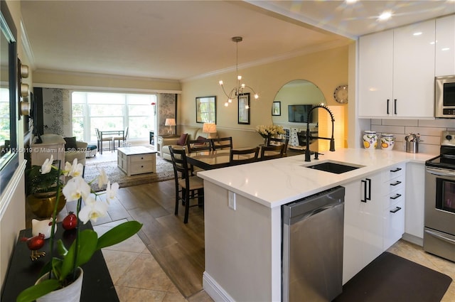 kitchen featuring ornamental molding, a sink, stainless steel appliances, a peninsula, and white cabinets