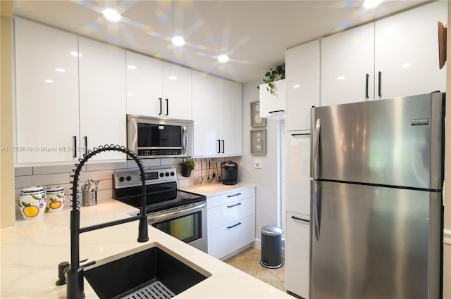 kitchen with backsplash, stainless steel appliances, white cabinetry, and sink